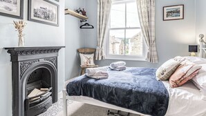 Une chambre à coucher avec un lit, une cheminée, une fenêtre avec des rideaux et des tableaux encadrés accrochés au mur.