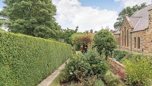Un jardin avec un bâtiment en pierre, une haie et un sentier.