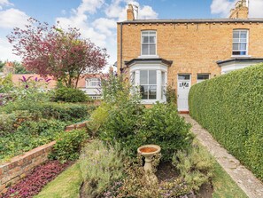 A brick house with a garden, a white door, and a window with a white frame.