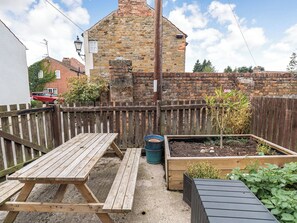 A wooden table and bench set in a garden with raised beds of plants.
