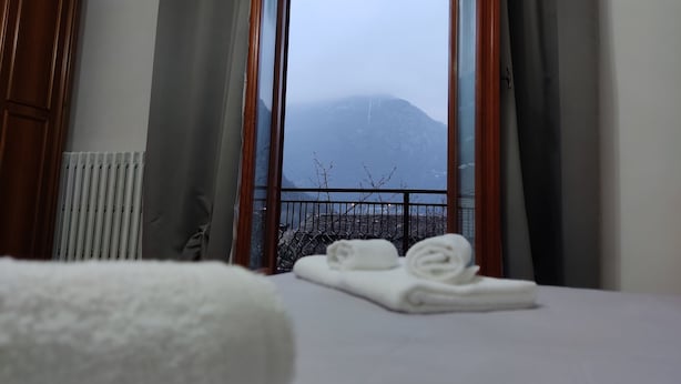 Une chambre d’hôtel avec un lit, une fenêtre donnant sur une montagne, un radiateur et une armoire en bois.