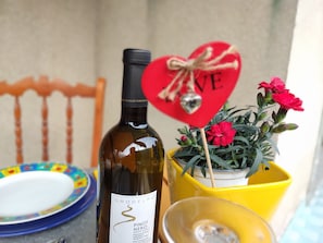 Une bouteille de vin, un objet décoratif en forme de cœur sur lequel est écrit le mot « AMOUR », une clochette et une plante en pot avec des fleurs rouges.