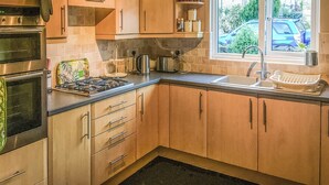 Une cuisine avec des meubles de rangement en bois, une cuisinière à gaz, un évier et une fenêtre donnant sur l’extérieur.