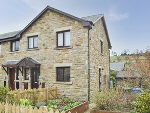 A stone house with a gabled roof, a wooden porch, and a garden with raised beds. - 3 bedroom accommodation in Rothbury (Rothbury)