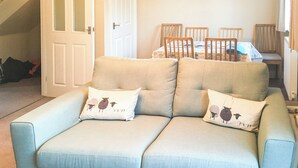 Un salon avec un canapé bleu clair, deux coussins assortis, une table à manger avec des chaises et un escalier en arrière-plan.