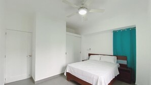 A bedroom with a bed, a ceiling fan, a door, and a teal curtain. - Your ideal vacation home in Sosua! (Sosúa)