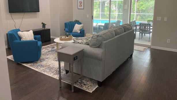 Ein geräumiges Wohnzimmer mit grauem Sofa, blauen Sesseln und einem an der Wand montierten Flachbildfernseher.