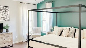 Ein modernes Schlafzimmer mit Himmelbett, Deckenventilator und Blick ins Freie durch große Fenster.