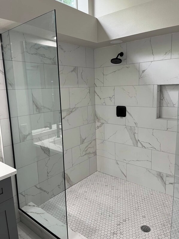 A modern bathroom with a glass shower enclosure, marble tiles, and a hexagonal tile floor. - Clean and modern home, sparkling heated pool, near river (Dunnellon)