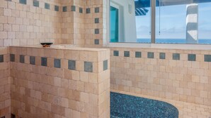 Ein Badezimmer mit beige- und dunkelblauen Fliesen, einem Fenster mit Ausblick und einer kleinen Schale auf einem Absatz.