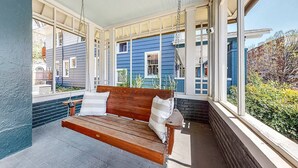 Un porche cubierto con una mecedora de madera, amplias ventanas y vistas a una casa azul.