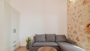 Ein modernes Wohnzimmer mit einem grauen Ecksofa, einem kleinen runden Holztisch und einer Topfpflanze.