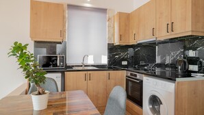 A compact kitchen with wooden cabinets, a marble countertop, a built-in washing machine, and a microwave.