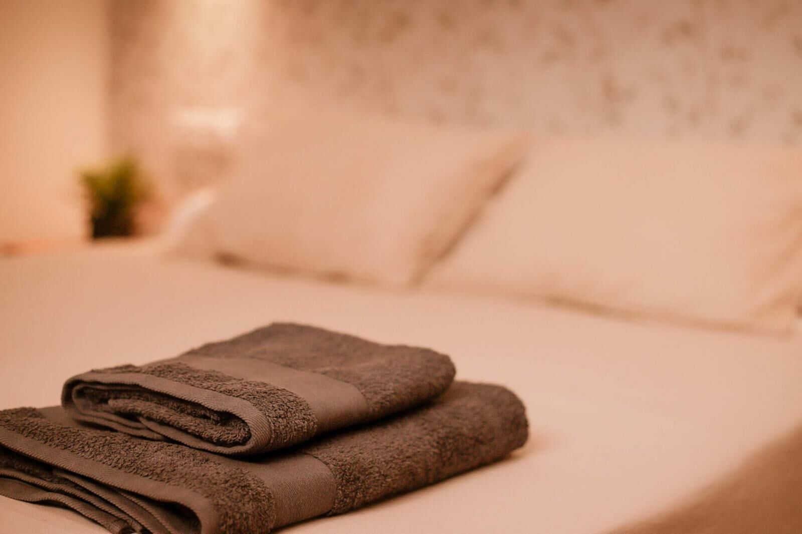 A neatly made bed with folded towels and a plain wall in the background.
