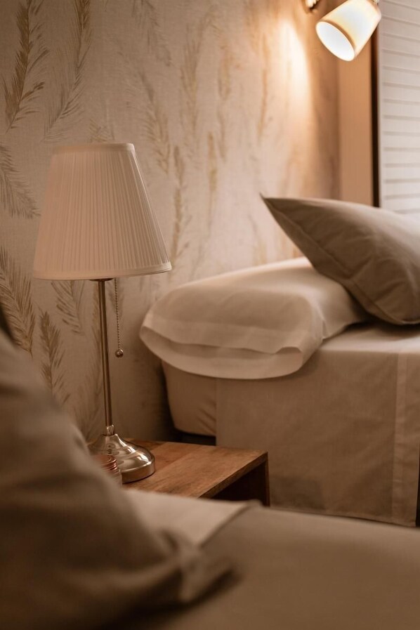 A bedroom with a bedside lamp, a wooden nightstand, and a bed with white bedding.
