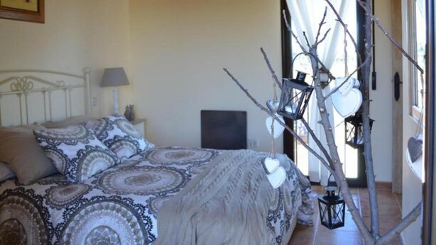 A bedroom with a bed, a nightstand, a lamp, a framed picture, and a window with curtains.
