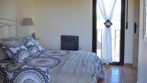 A bedroom with a bed, a nightstand, a lamp, and a view of the outside through a door.