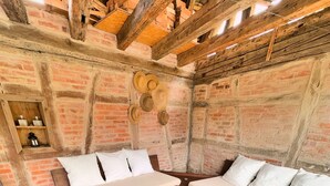 A rustic room with exposed brick walls, wooden beams, a bed with white bedding, a wooden table, and a woven basket. - Gîte Le Chut - Jacuzzi & Swimming pool - 22km Strasbourg (Rangen)