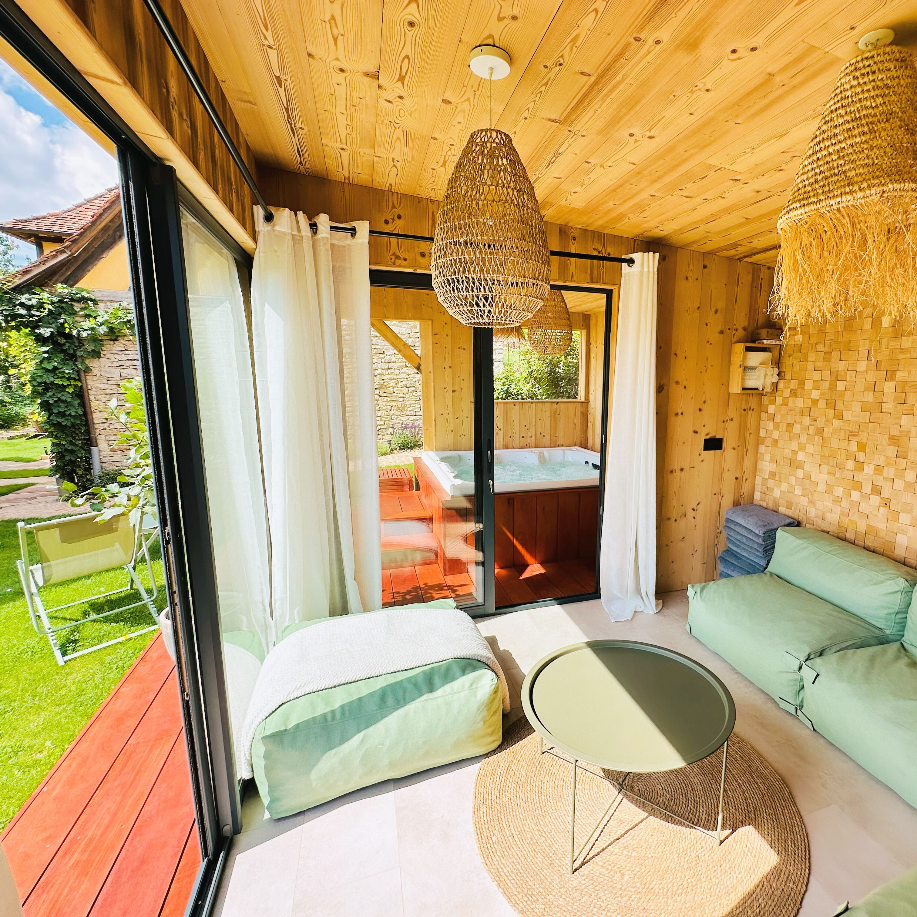 A cozy room with a wooden ceiling, a green sofa, a small round table, and a wicker hanging light fixture.