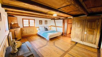 Een rustieke slaapkamer met een houten plafond, een bed met een blauwe deken, houten kasten en een klein beeldje op een tafel.