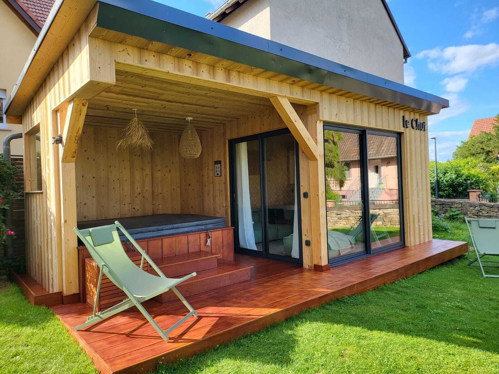 Une structure extérieure en bois, dotée d’un banc et d’une porte vitrée donnant sur un patio abrité.