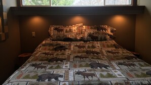 Un lit recouvert d’une courtepointe à motifs animaliers, une fenêtre au-dessus du lit et un luminaire fixé au mur.