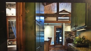 Un couloir étroit, avec un plancher et des murs en bois, qui mène à un espace cuisine doté d’un mur en pierre et d’un évier.