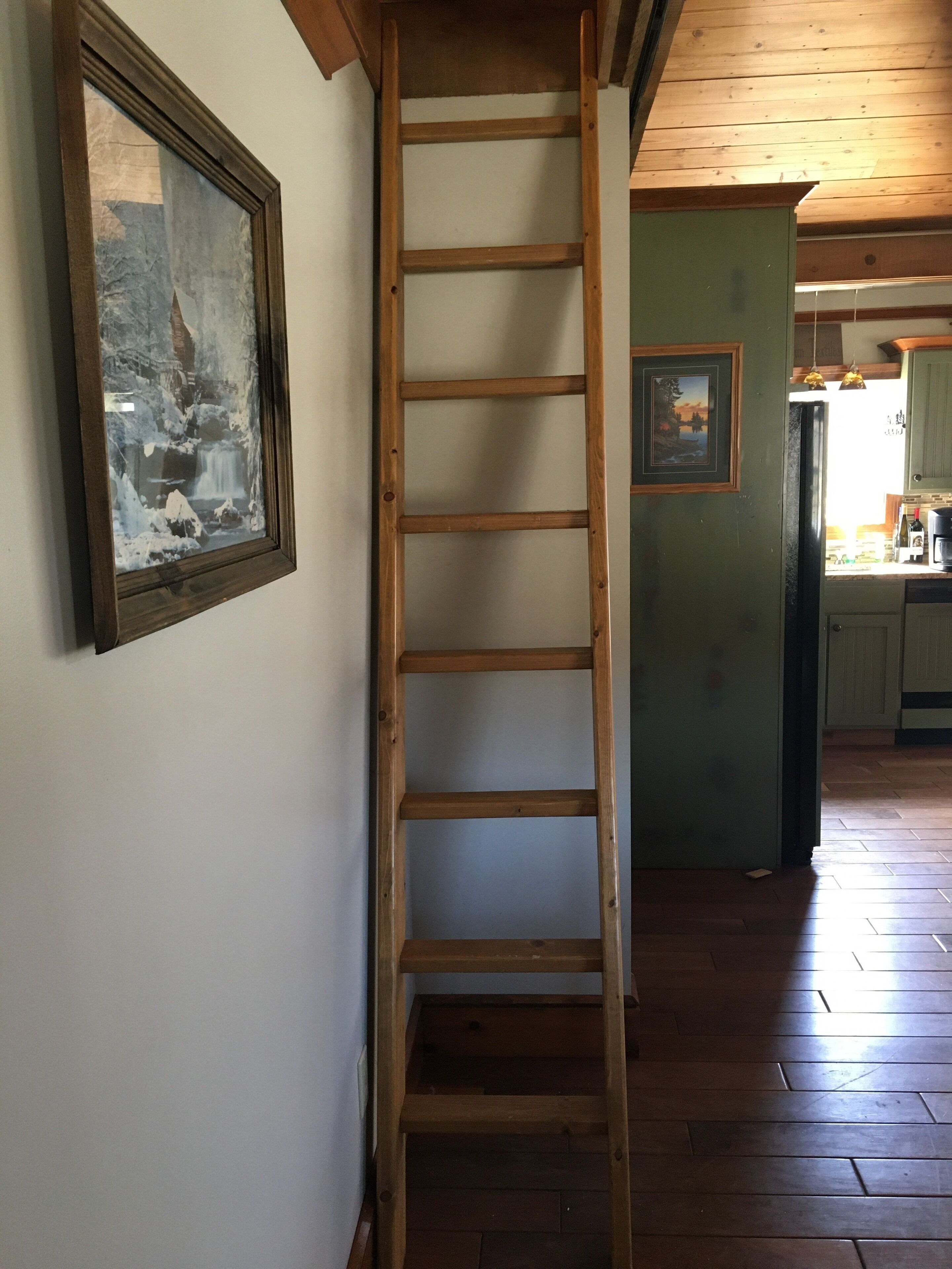 A wooden ladder against a wall with a framed picture.