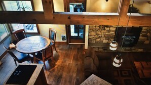 Une pièce aux hauts plafonds, dotée d’une cheminée en pierre, d’un plancher en bois et d’un coin repas avec une table ronde et des chaises.