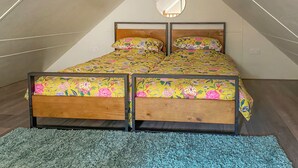 Un dormitorio con techo inclinado, una cama con ropa de cama floral, un espejo redondo y una alfombra azul.