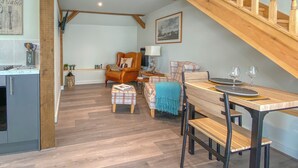 Un amplio salón con escalera de madera, una mesa de comedor para dos personas y una acogedora zona de estar.