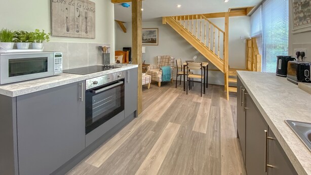 Una cocina moderna con microondas integrado, horno y pileta. Una escalera de madera conduce a un comedor con mesa y sillas.