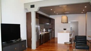 Uma sala de estar moderna com televisão de tela plana, piso de madeira, área de jantar com mesa e cadeiras, e cozinha com eletrodomésticos de aço inoxidável.