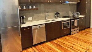 Uma cozinha moderna com eletrodomésticos de aço inoxidável, piso de madeira e armários escuros.