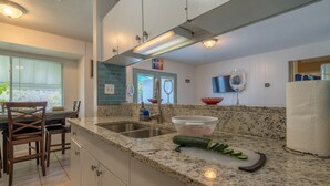 Cocina con encimeras de granito, pileta de acero inoxidable y comedor con sillas de madera.