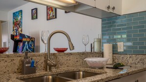 Una cocina con encimeras de granito, un lavamanos de acero inoxidable, dispensador de jabón, colador y botella de jabón.