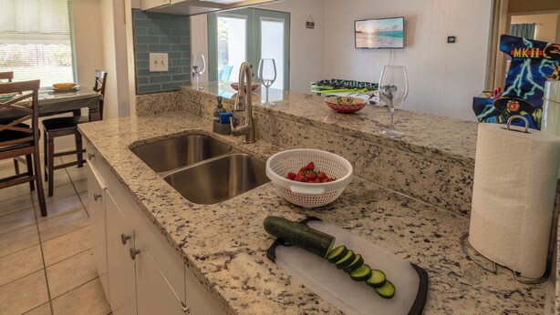 Una cocina con encimeras de granito, un fregadero y una tabla de cortar con pepinos en rodajas.
