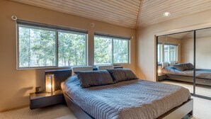 A modern bedroom with a large bed, two bedside tables, and a large window providing a view of trees. - Modern Sunriver Luxury Home with Fenced Turf Pet Yard, Large Kids Room, SHARC !! (Sunriver)