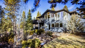A modern two-story house with a deck, surrounded by a forested landscape. - Modern Sunriver Luxury Home with Fenced Turf Pet Yard, Large Kids Room, SHARC !! (Sunriver)