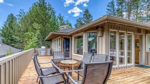 A wooden deck with outdoor furniture, a glass-enclosed patio, and a view of the surrounding forest. - Modern Sunriver Luxury Home with Fenced Turf Pet Yard, Large Kids Room, SHARC !! (Sunriver)
