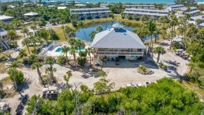 Eine Vogelperspektive zeigt einen luxuriösen Urlaubsort mit mehreren Gebäuden, einem zentral gelegenen Pool und umliegenden Palmen.