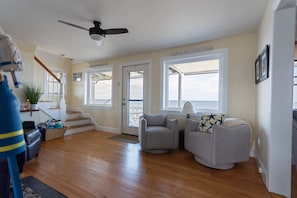 A spacious living room with hardwood floors, a ceiling fan, and large windows.