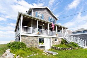 A two-story house with a porch, a stone foundation, and a flag.
