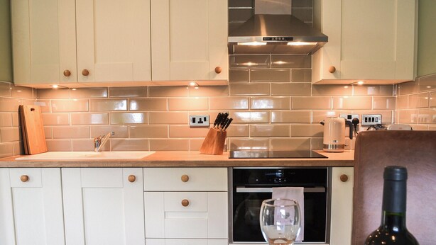A modern kitchen with white cabinets, a stainless steel range hood, and a wooden countertop. - The Hen House - UK38436 (Bridlington)