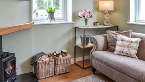 A cozy living room with a fireplace, a sofa, a table with a lamp, and a window with curtains. - The Hen House - UK38436 (Bridlington)