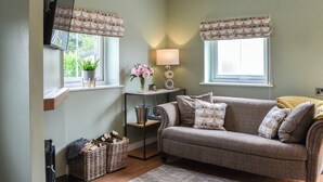 A cozy living room with a sofa, two windows with curtains, a lamp, a small table, and a plant. - The Hen House - UK38436 (Bridlington)