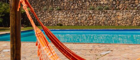 A hammock by a stone wall and a swimming pool.