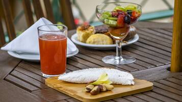 A wooden table with a glass of red drink, a fruit bowl, and a plate of pastries.