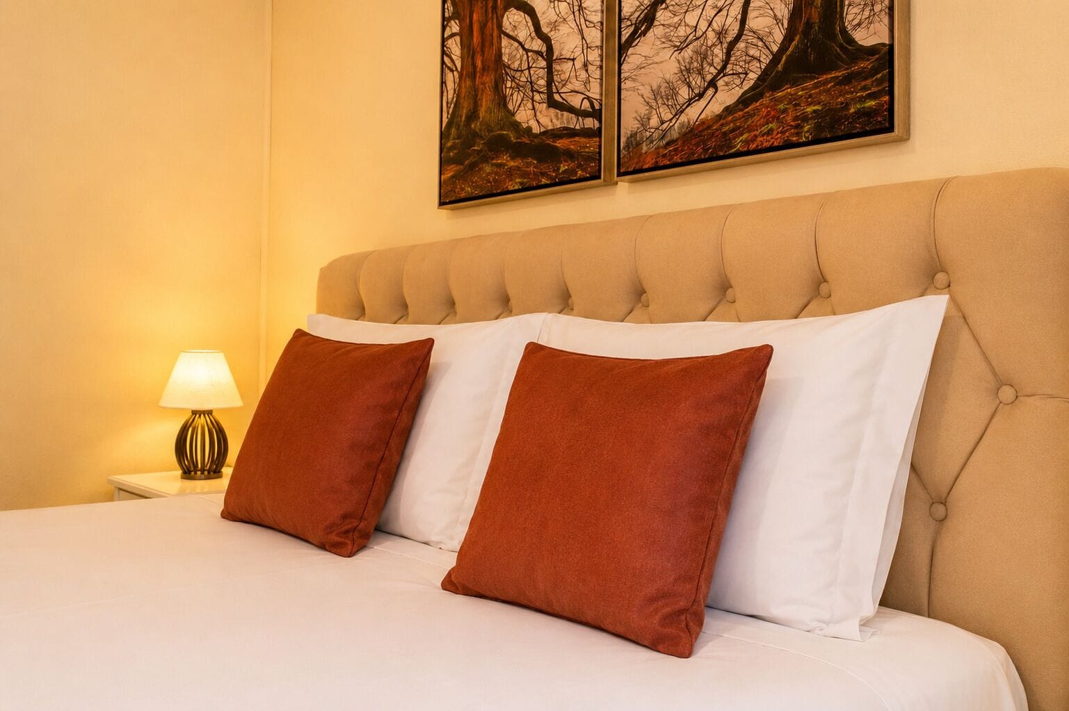 A bed with a tufted headboard, two pillows, a bedside lamp, and a framed artwork above.
