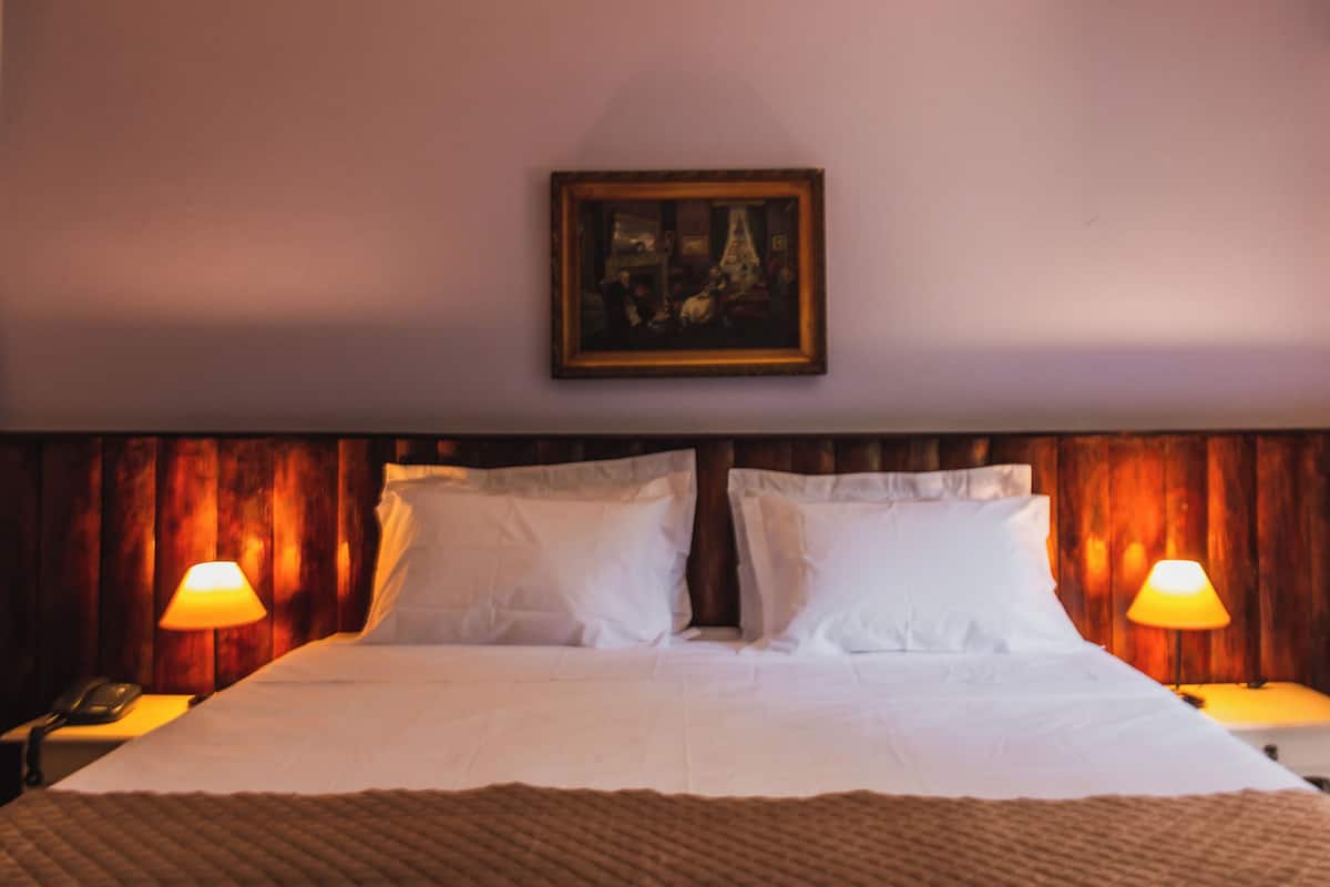 A hotel room with a large bed, two bedside lamps, a framed picture on the wall, and wooden paneling on the walls.